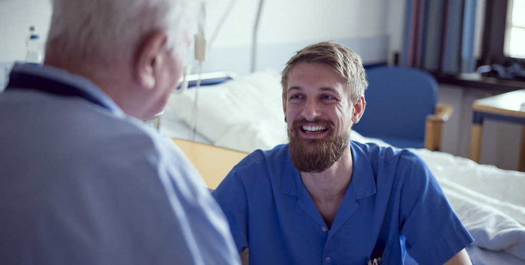 Ein Pfleger lächelt einem älteren Patienten zu 